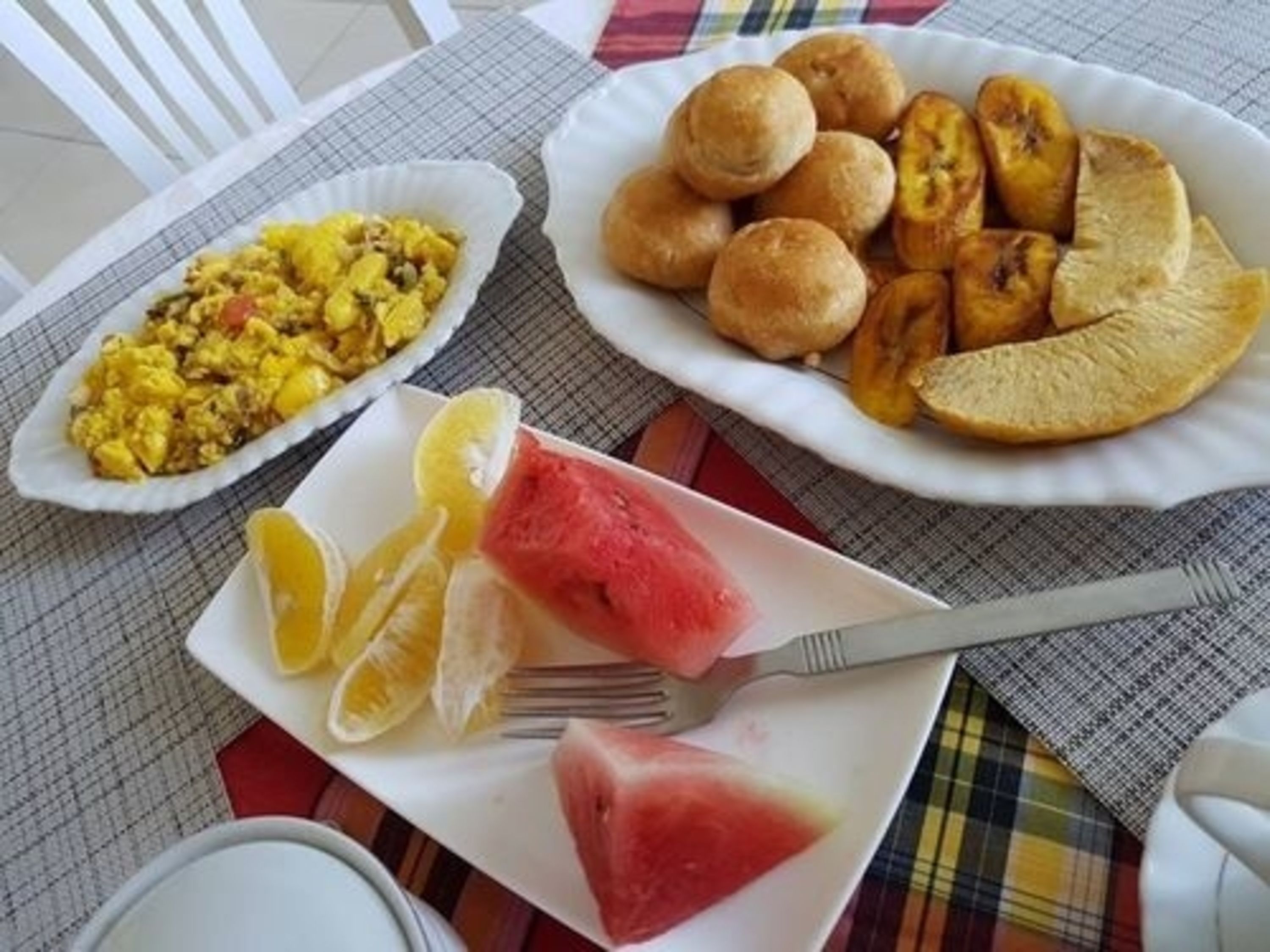 Una mesa con un plato de huevos revueltos, un plato de plátanos fritos y un plato de rebanadas de sandía.