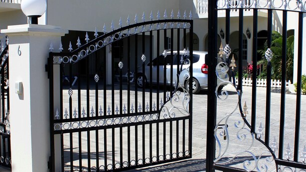 A gated entrance with a decorative iron gate, a white building with arched windows, and a red roof.