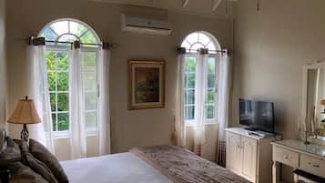 A bedroom with a bed, a TV, a dresser, and two windows with curtains.