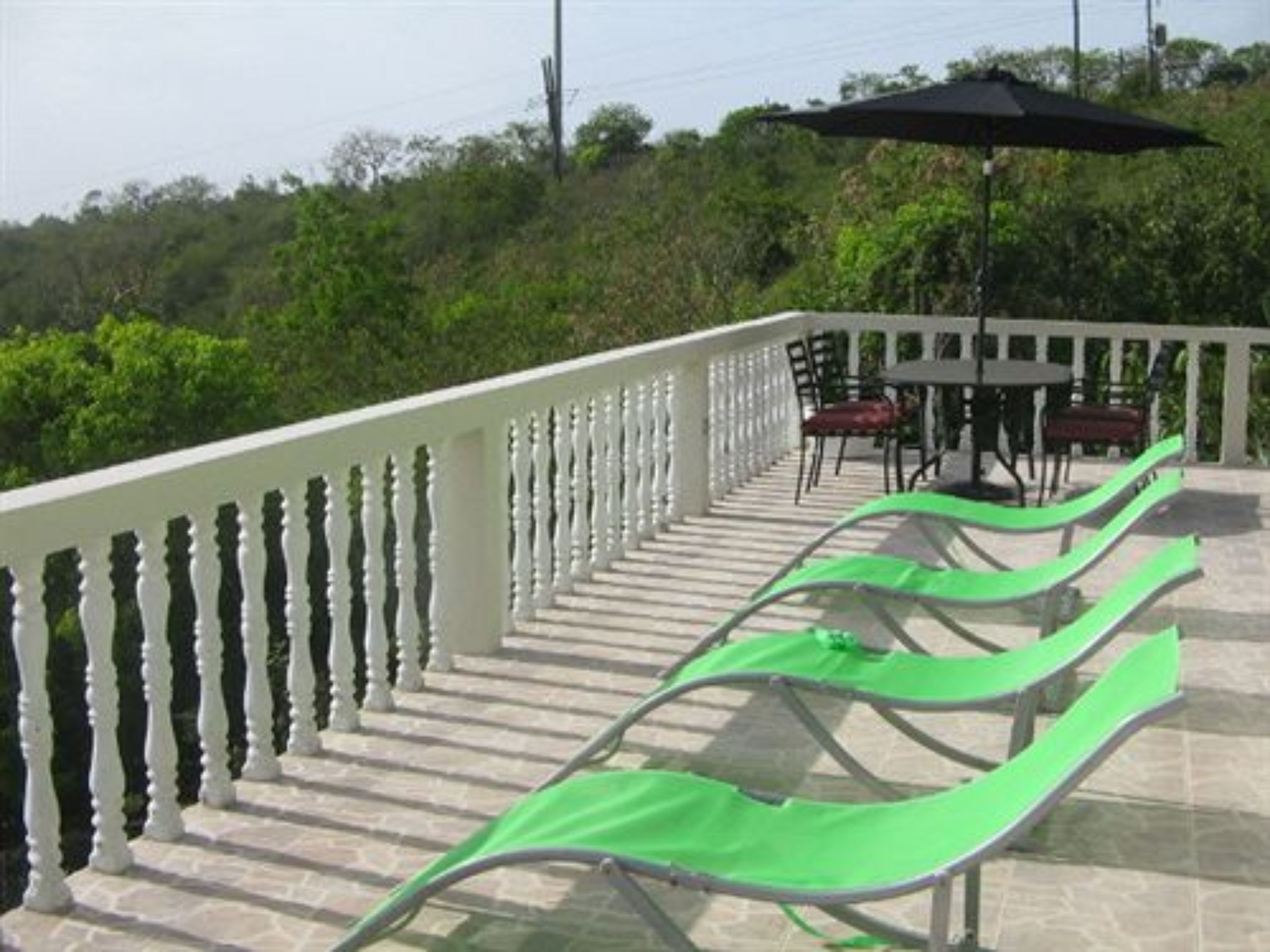 A balcony with white balustrades, green lounge chairs, a table with chairs, and an umbrella.