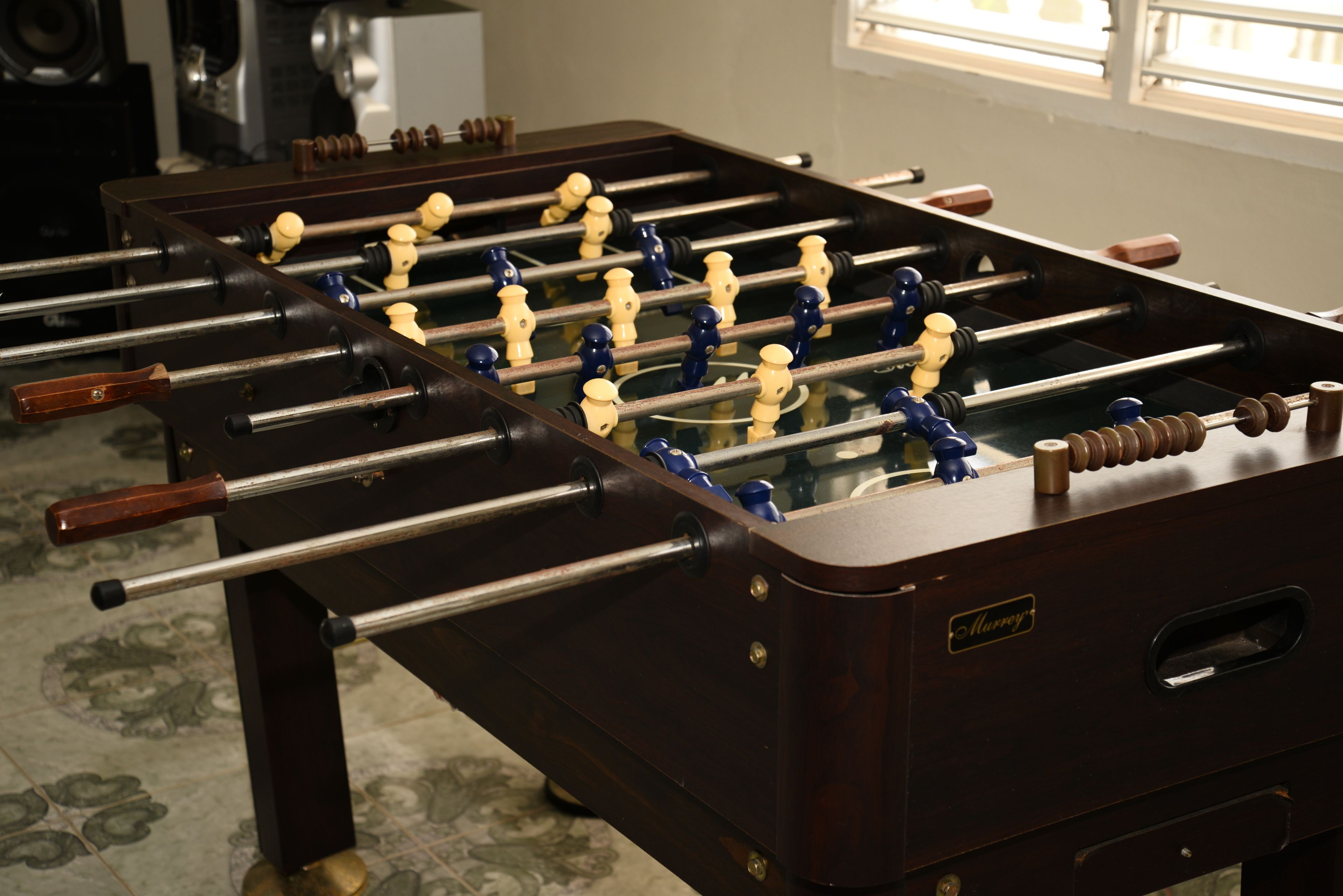 A Foosball table with a dark wooden finish and a brand name visible.