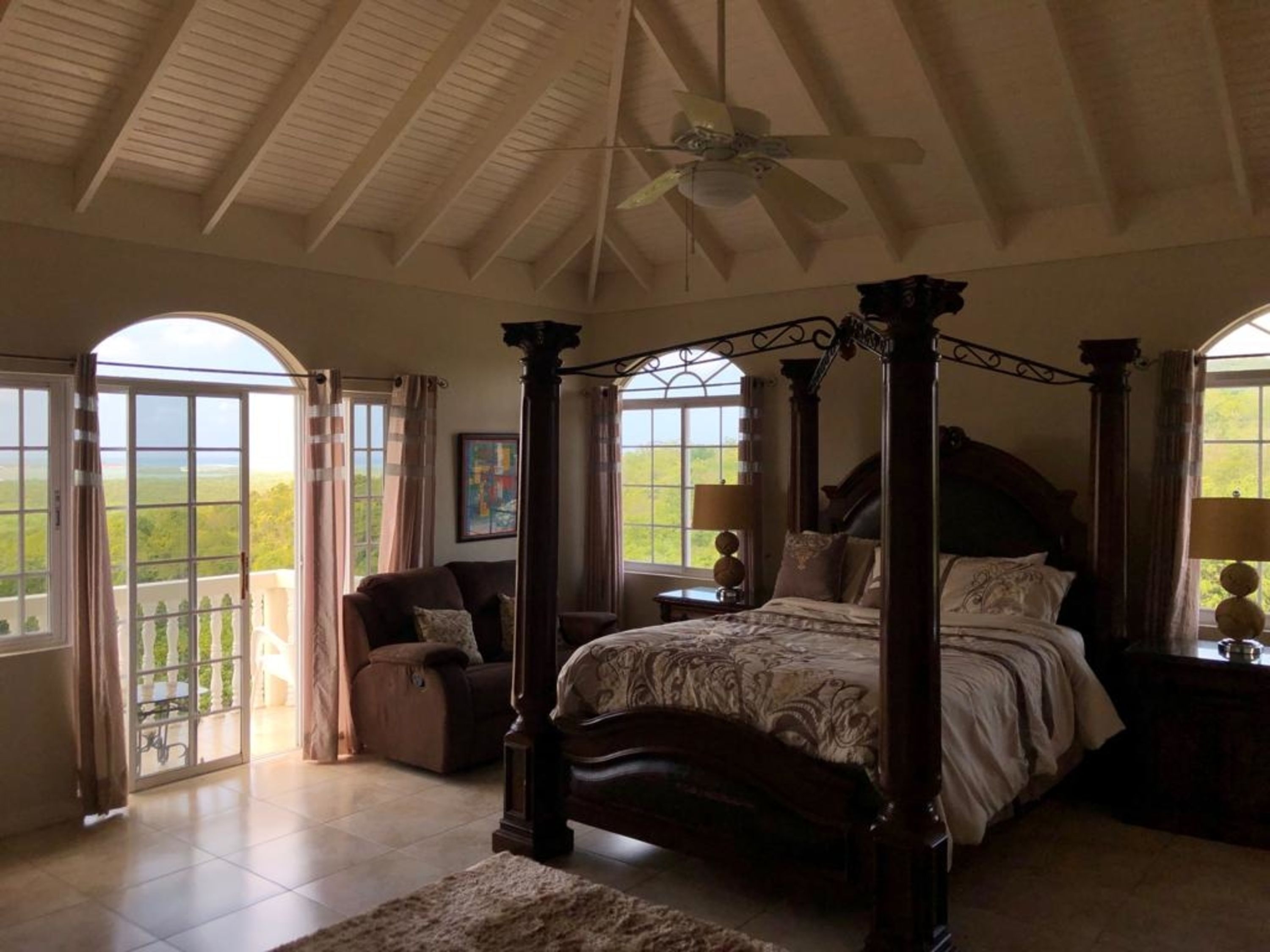 A spacious bedroom with a four-poster bed, large windows, and a balcony.
