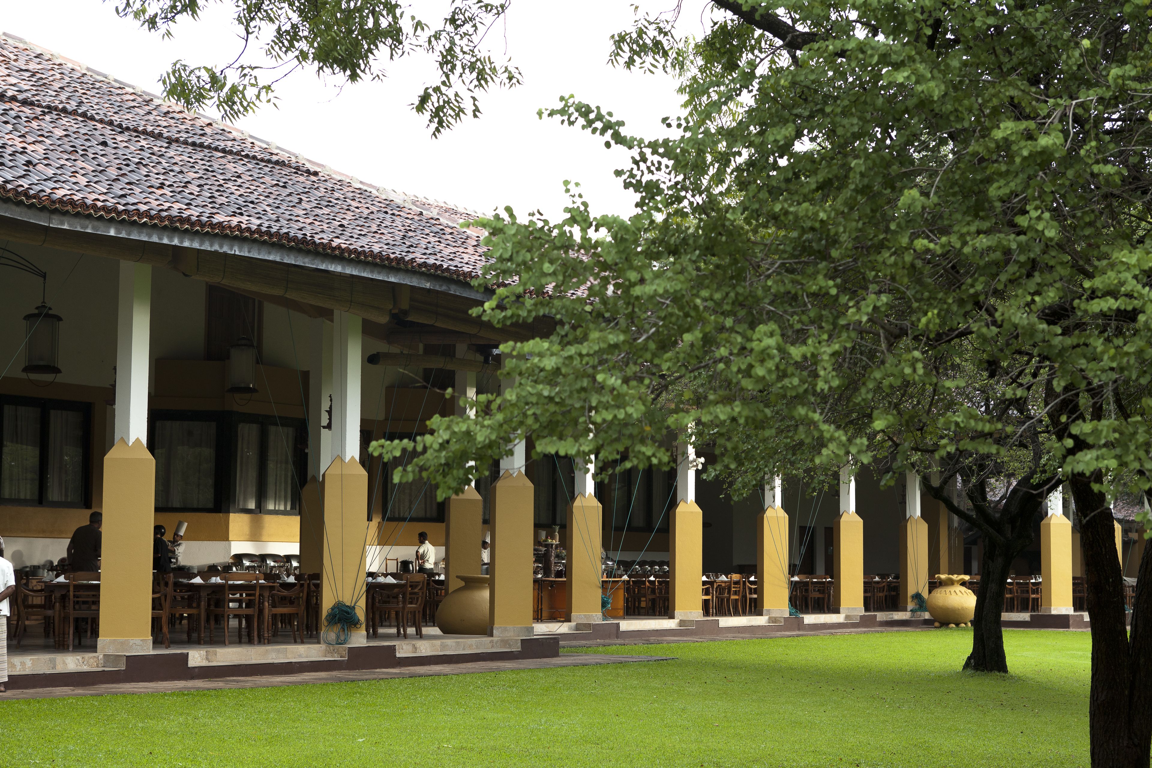 A building with a tiled roof and columns, surrounded by a well-maintained lawn and trees.