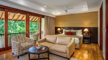 A spacious bedroom with a large bed, a sitting area with a sofa and armchairs, a dining table, and a balcony with a wooden railing.