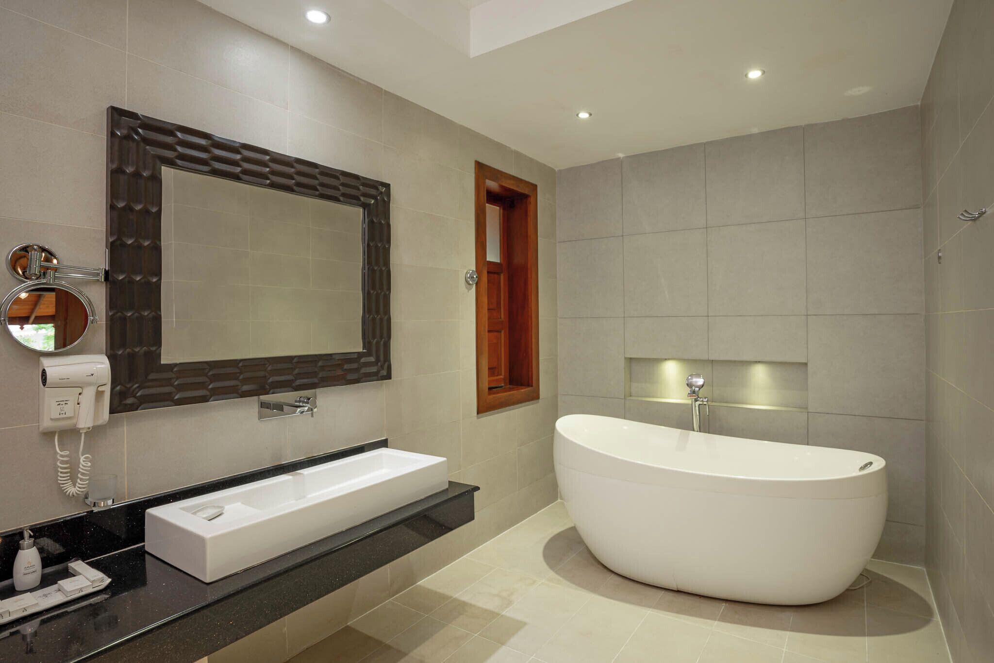 A modern bathroom with a freestanding bathtub, a large mirror, and a vanity with a sink and phone.