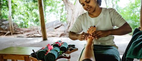 A person receiving a foot massage outdoors with a bench and rolled towels nearby.