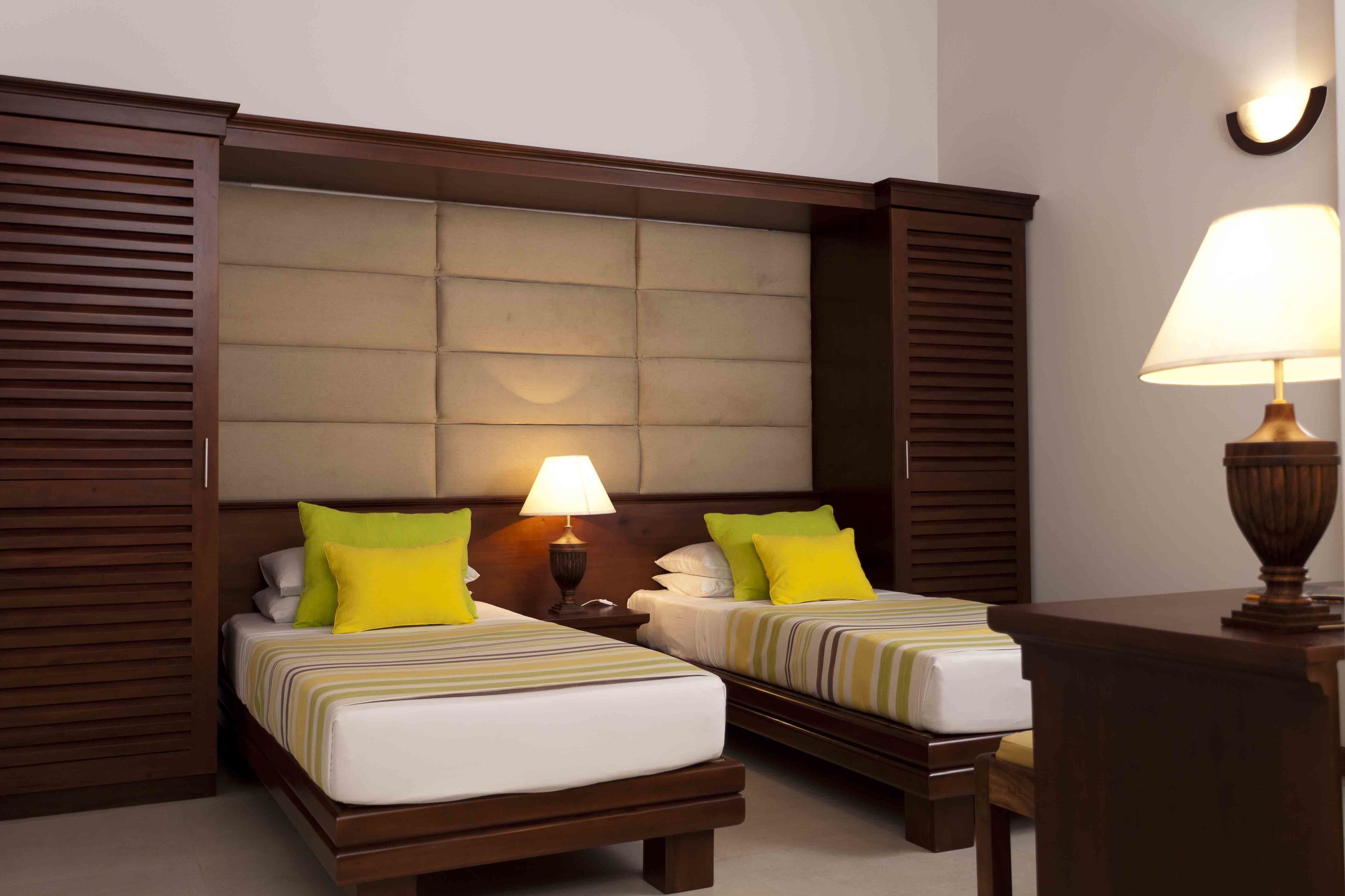 A hotel room with two beds, a nightstand with a lamp, and a wooden desk.