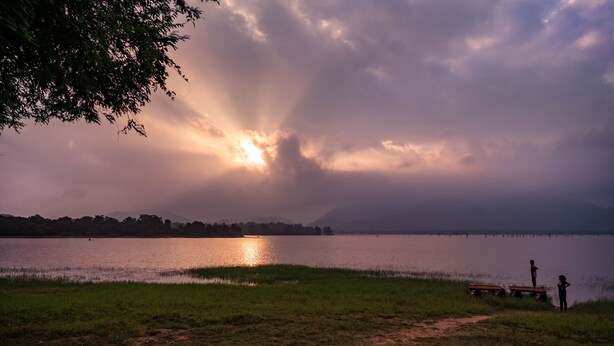 A lakeside view with a path leading to a dock, a bench, and two people standing by the water. - Amaya Lake Dambulla (Kandalama)