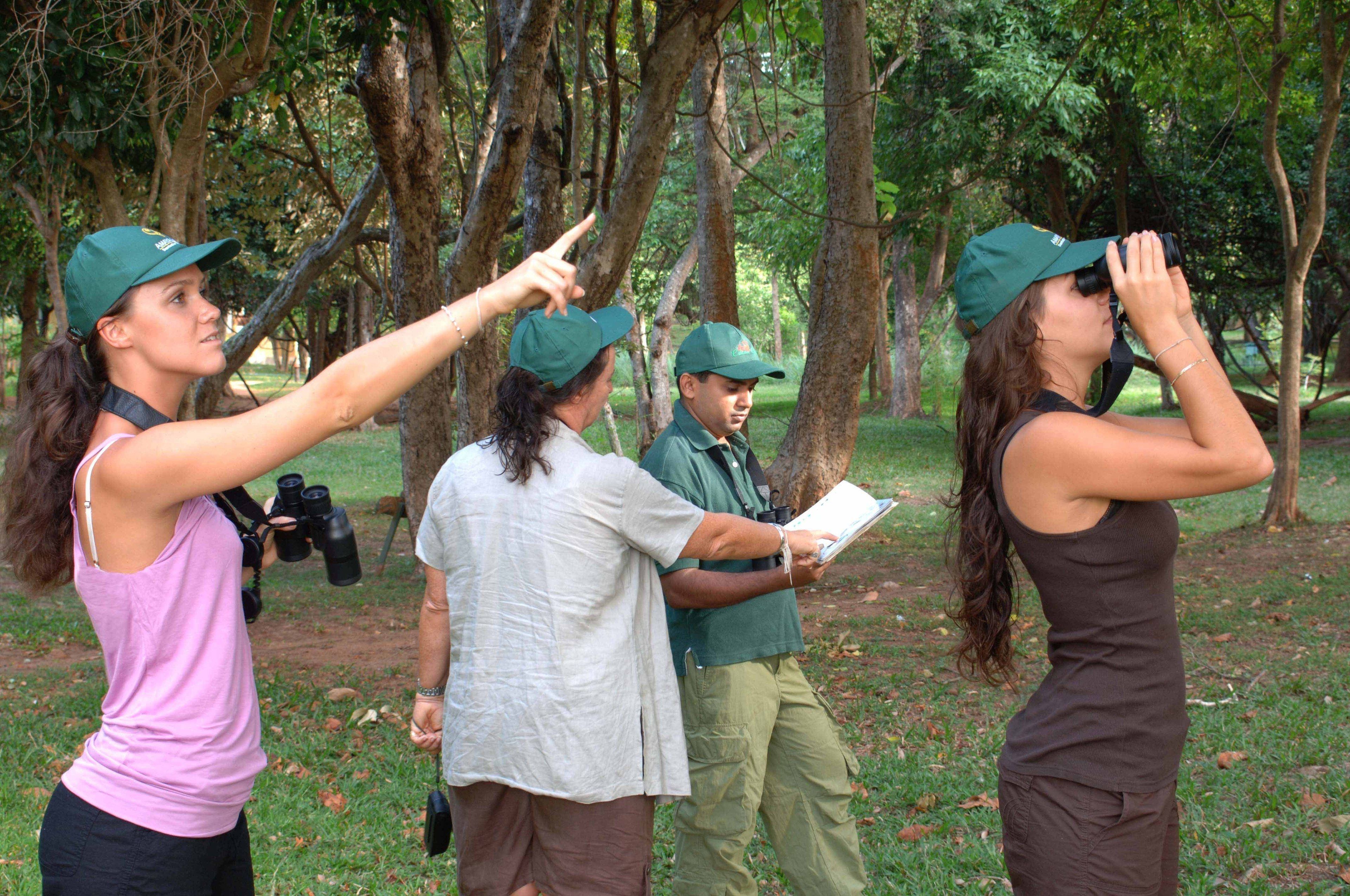 A group of people in a wooded area, some holding binoculars and pointing.
