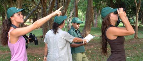 A group of people in a wooded area, some holding binoculars and pointing.
