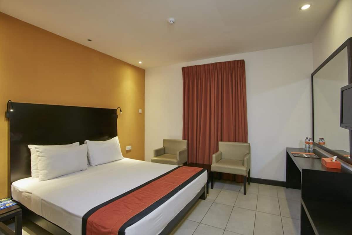 Une chambre d’hôtel comprenant un lit, un bureau, deux chaises, une télévision et une fenêtre avec des rideaux.