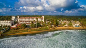 Un hotel frente al mar con varias edificaciones, una playa y olas oceánicas.