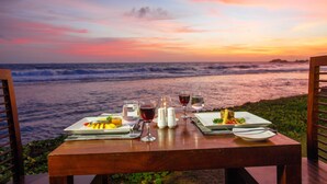 Una mesa dispuesta con platos de comida y copas de vino, con vista al océano al atardecer.