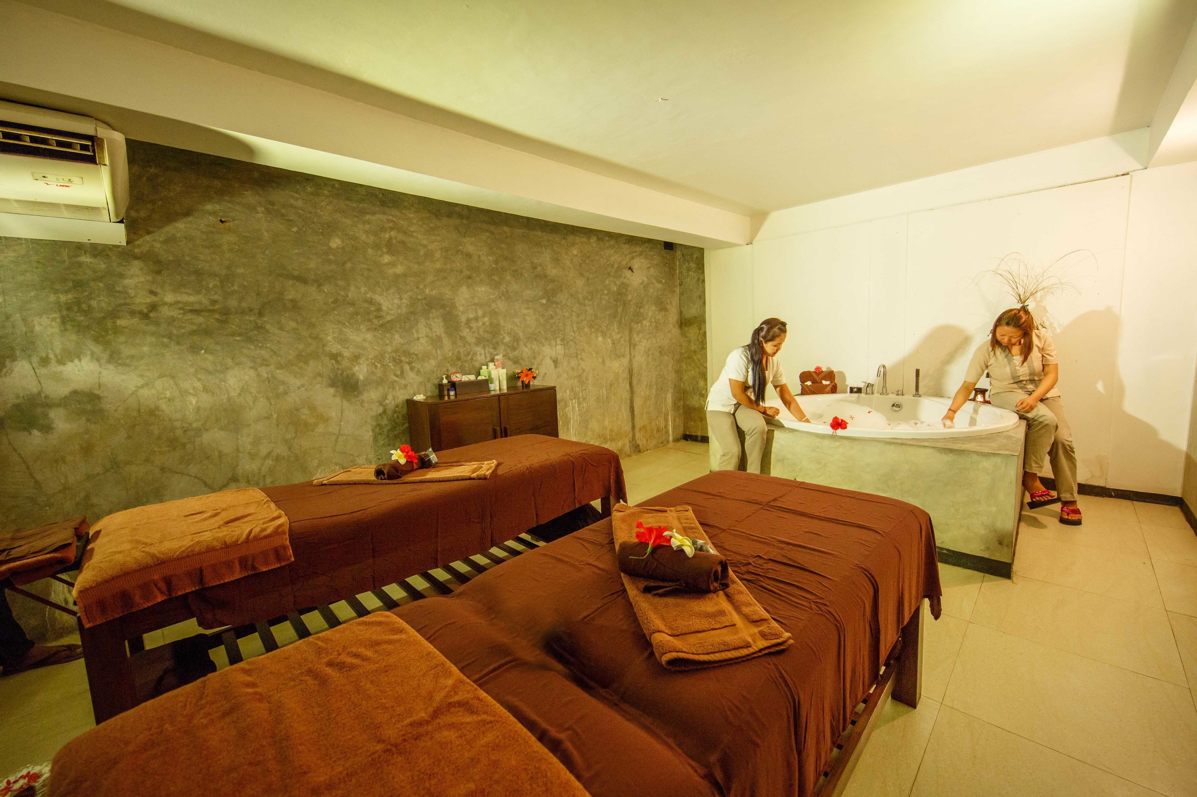 A spa room with two massage tables, a bathtub, and a small shelf with toiletries.