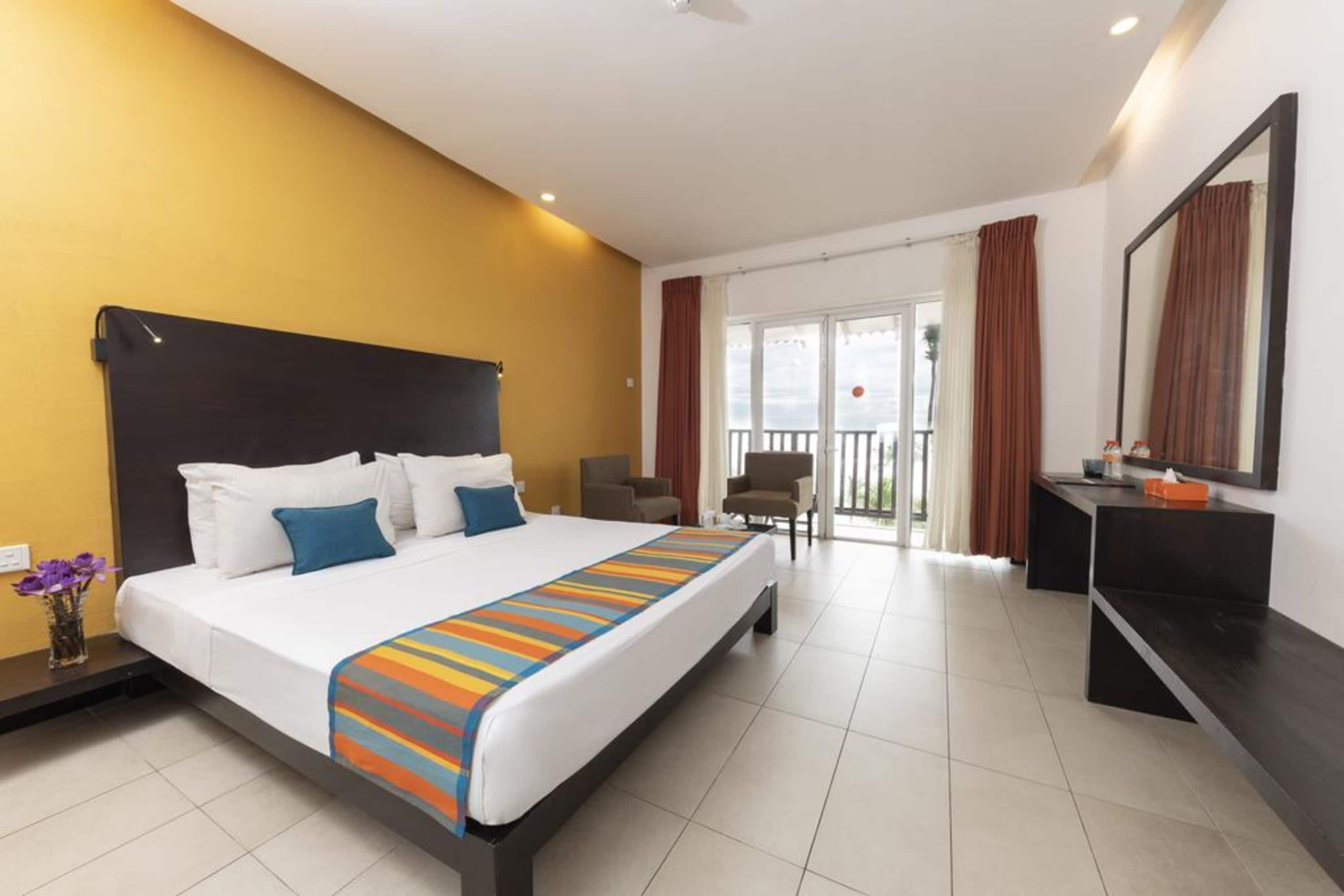 A hotel room with a large bed, a desk, a chair, and a balcony with curtains.