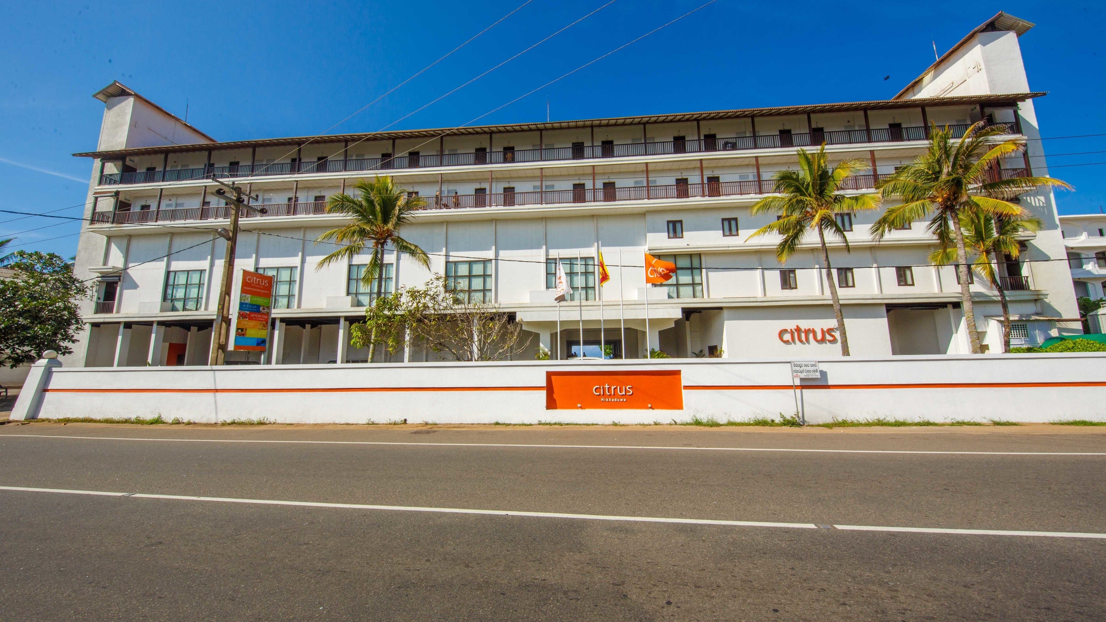 Un hôtel à plusieurs étages doté de balcons, de palmiers et d’une grande enseigne représentant des agrumes.