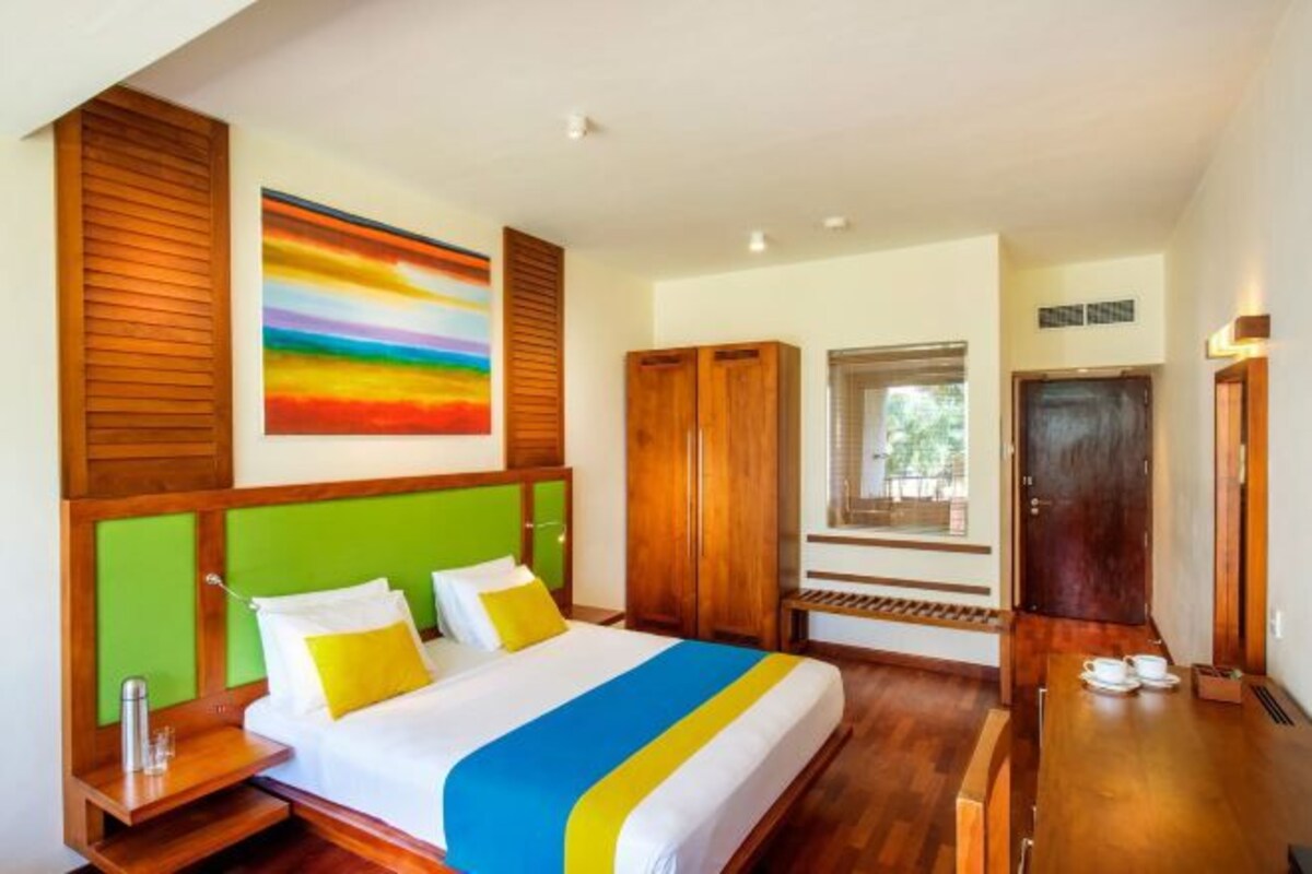 A hotel room with a bed, wooden headboard, a painting, a wardrobe, and a window.