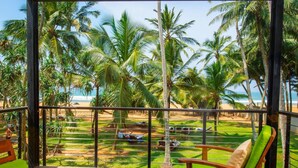 A balcony with a view of a beach, palm trees, and a pool area. - Mermaid Hotel & Club (Wadduwa)