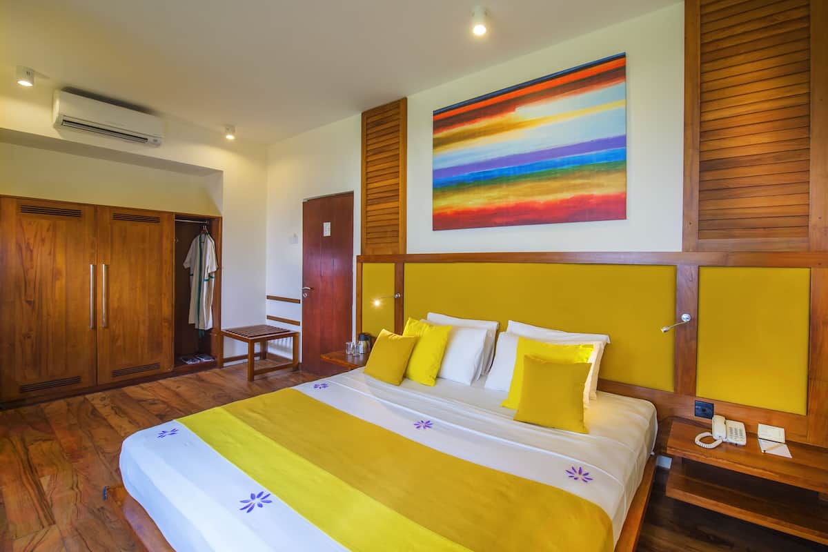A hotel room with a large bed, wooden wardrobe, and a colorful painting on the wall.