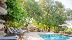Un espace aménagé au bord de la piscine, avec des chaises longues et un mur en pierre.