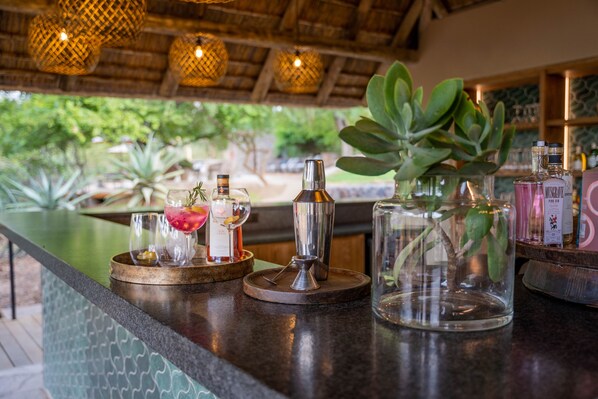 A bar area with a counter, cocktail glasses, a cocktail shaker, and a potted plant. - Thornybush Game Lodge (Hoedspruit)