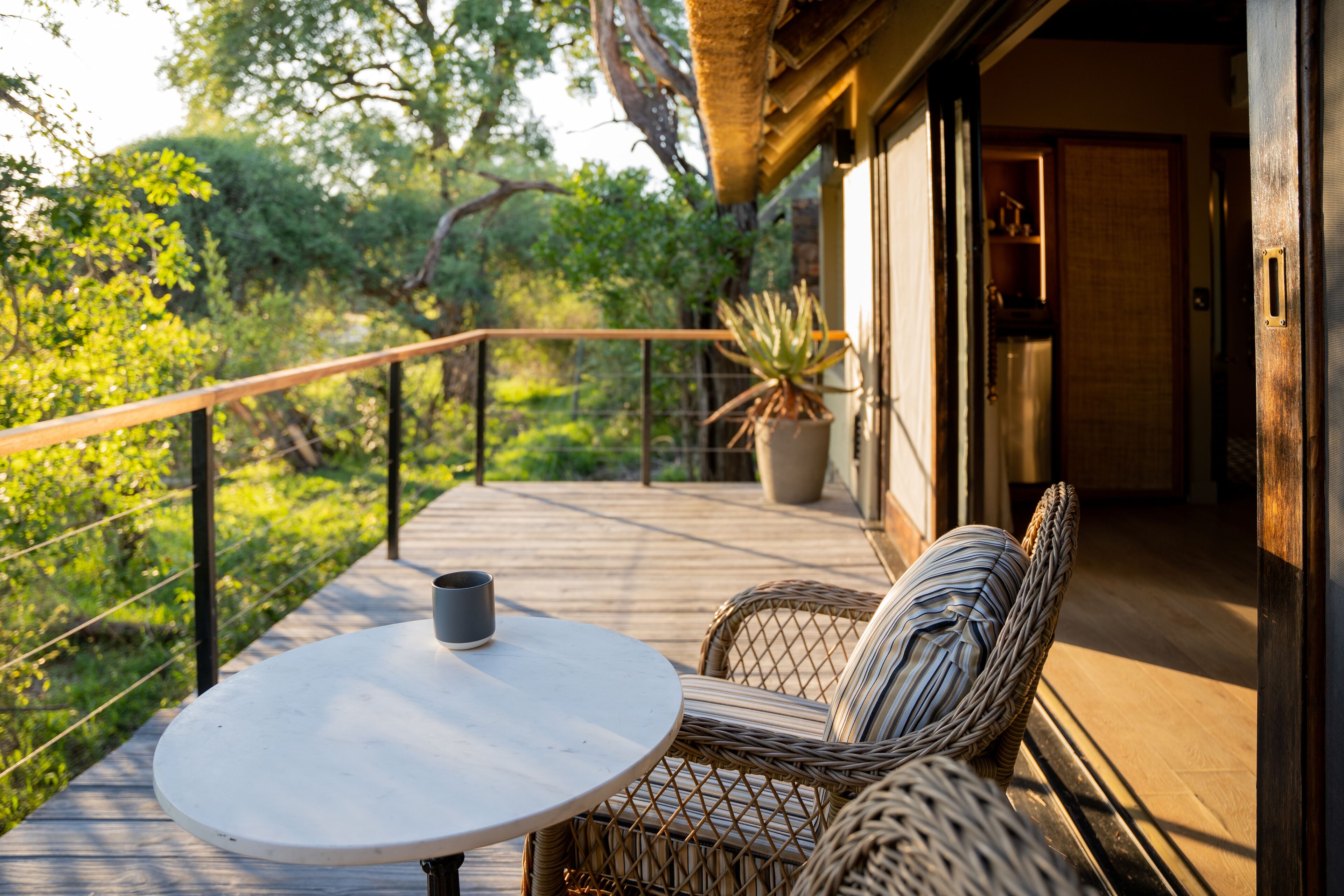 Ein Balkon mit Korbmöbeln und einem Tisch, mit Blick auf einen üppigen Garten.