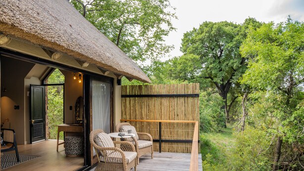 Une terrasse en bois avec des meubles en osier, un toit de chaume et une vue sur une végétation luxuriante.
