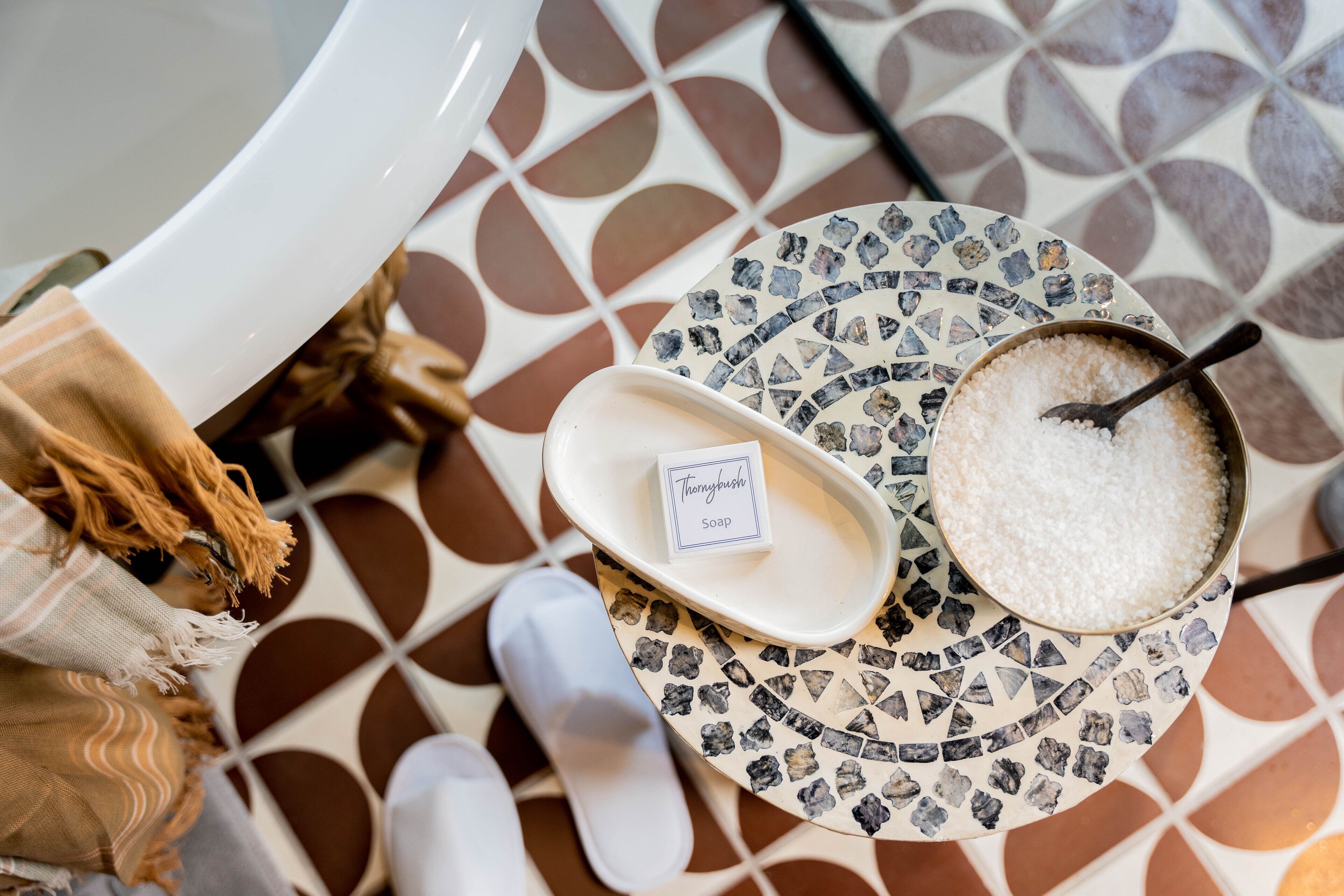 A bathroom with a white bathtub, a basin with a label reading "Thermybath Soap," and a bowl of white bath salts.