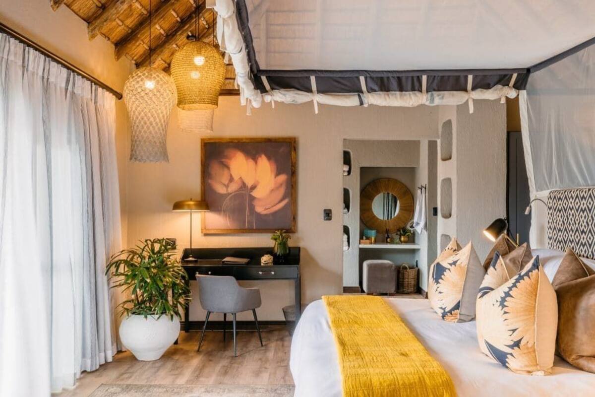 A bedroom with a bed, bedside table, lamp, and a desk with a chair.
