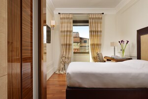A hotel room with a bed, a desk with a lamp, a chair, and a view of buildings through the curtains.
