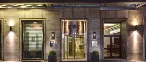 A hotel entrance with numbered doors, a revolving door, and two potted plants.