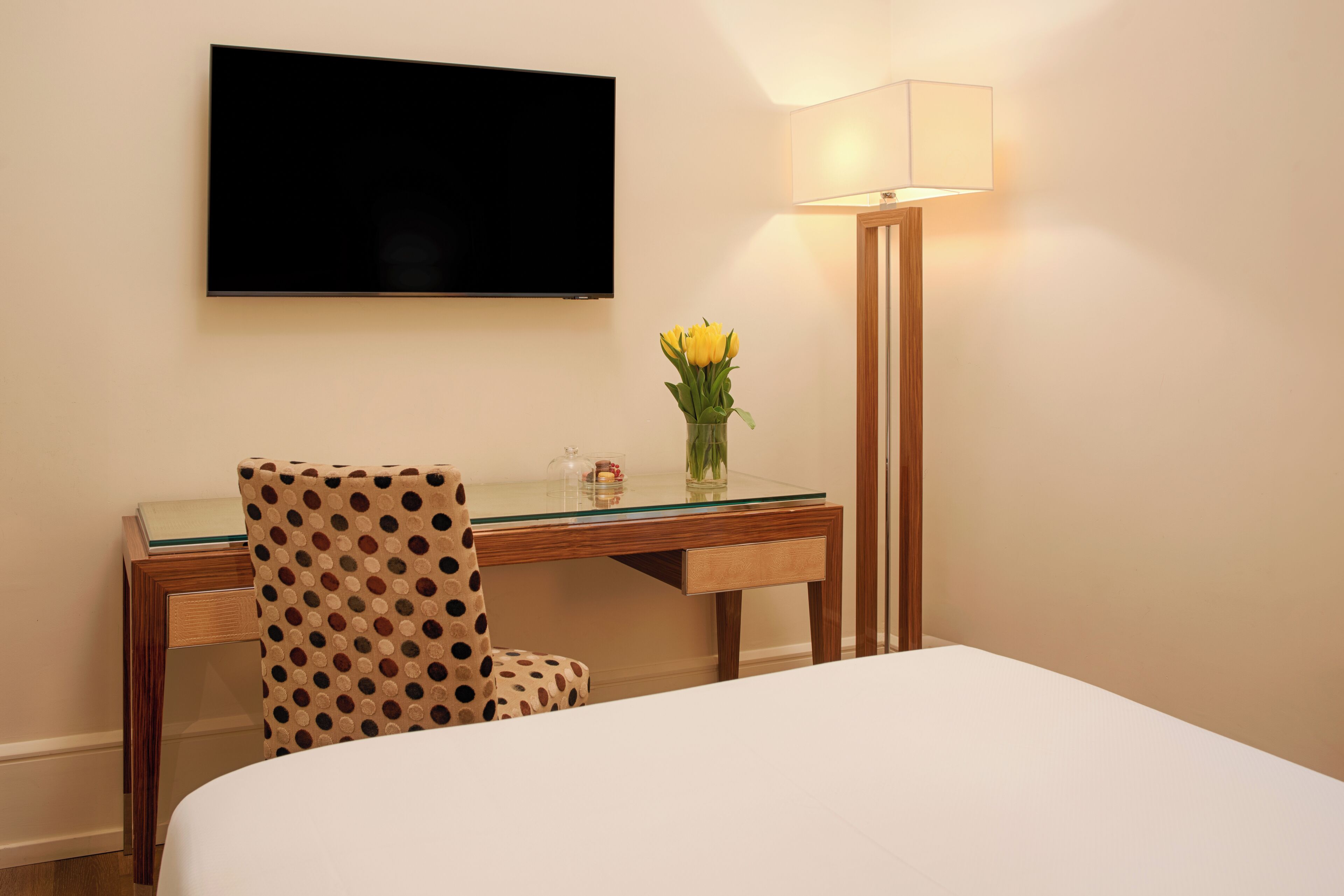 Habitación de hotel con cama, escritorio, silla, televisor montado en la pared y lámpara.