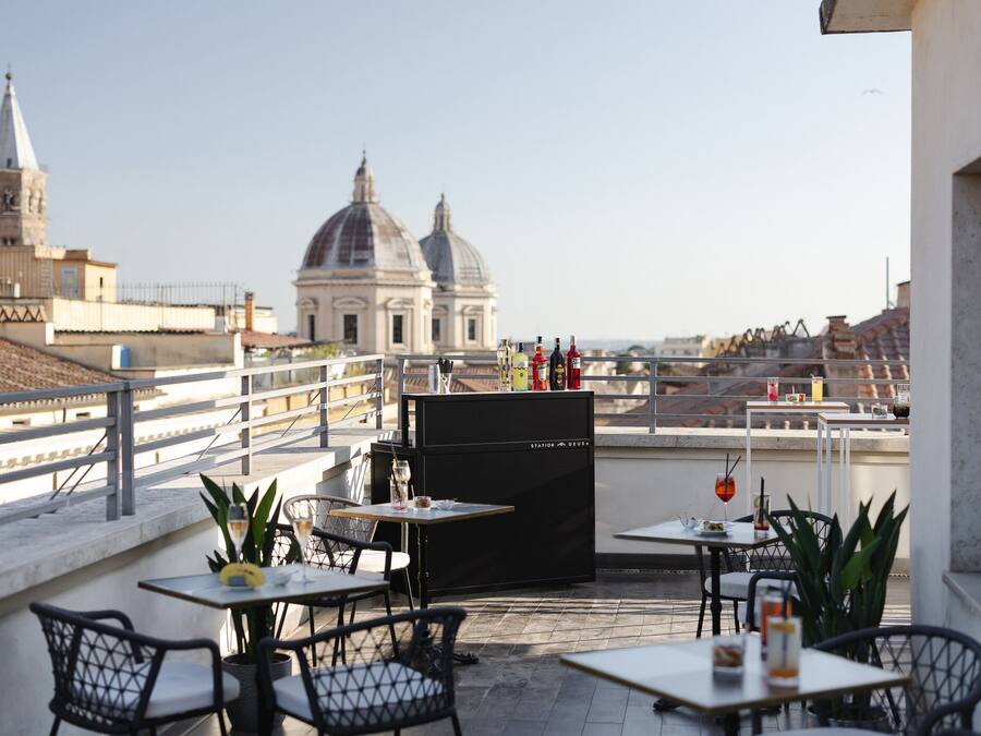 Une terrasse avec des tables et des chaises, un meuble noir et, au loin, une vue sur un grand bâtiment en forme de dôme.