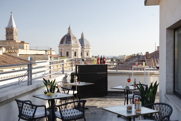 A terrace with tables and chairs, a black cabinet, and a view of a large dome building in the background.