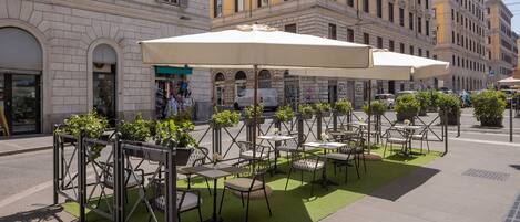 An outdoor seating area with tables and chairs, surrounded by a low fence and potted plants.