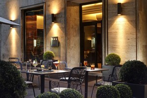 An outdoor dining area with tables and chairs, a sign with the name 'ANA', and decorative lighting.