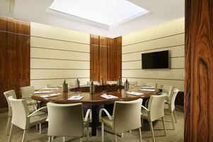 A conference room with a round table, white chairs, a flat-screen TV on the wall, and wooden paneling on the walls.
