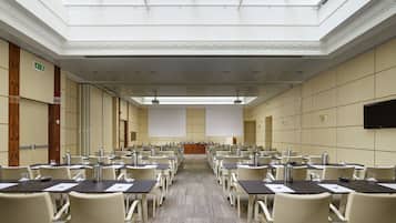 A conference room with rows of tables and chairs, a podium, and a large screen at the front.