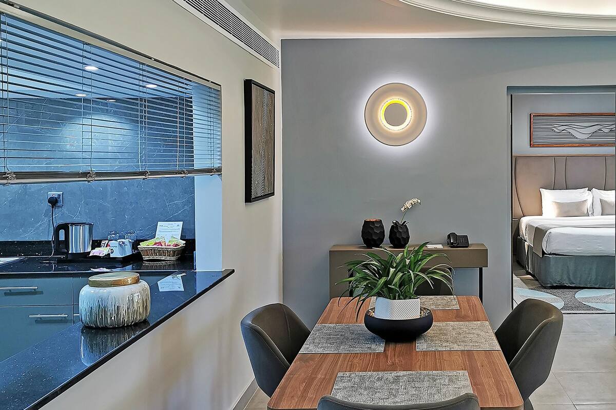 A modern kitchen with a built-in island, a dining area with a wooden table and chairs, and a bedroom with a bed and nightstand.