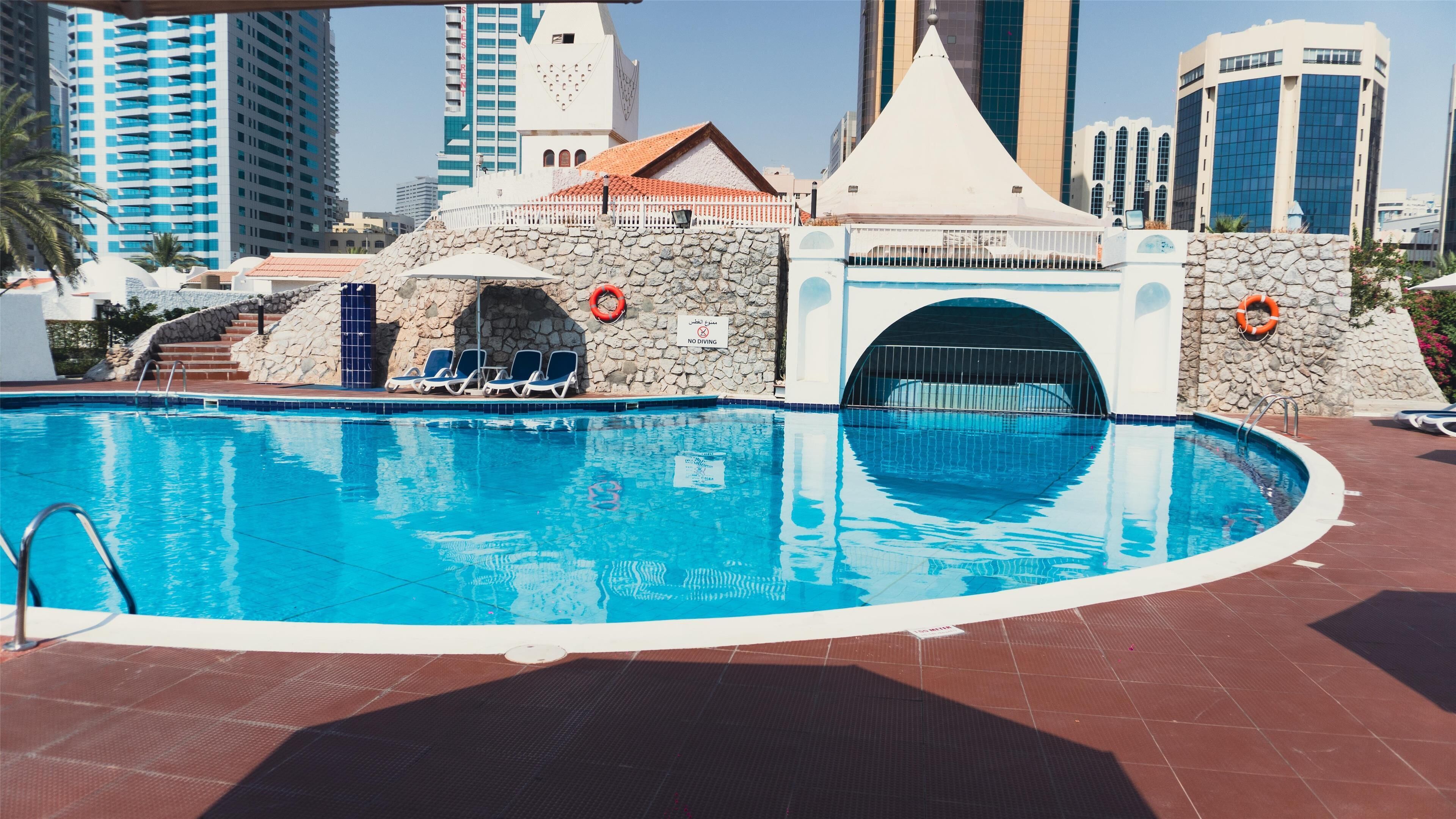A swimming pool with lounge chairs, a no diving sign, and a stone wall with a covered entrance.