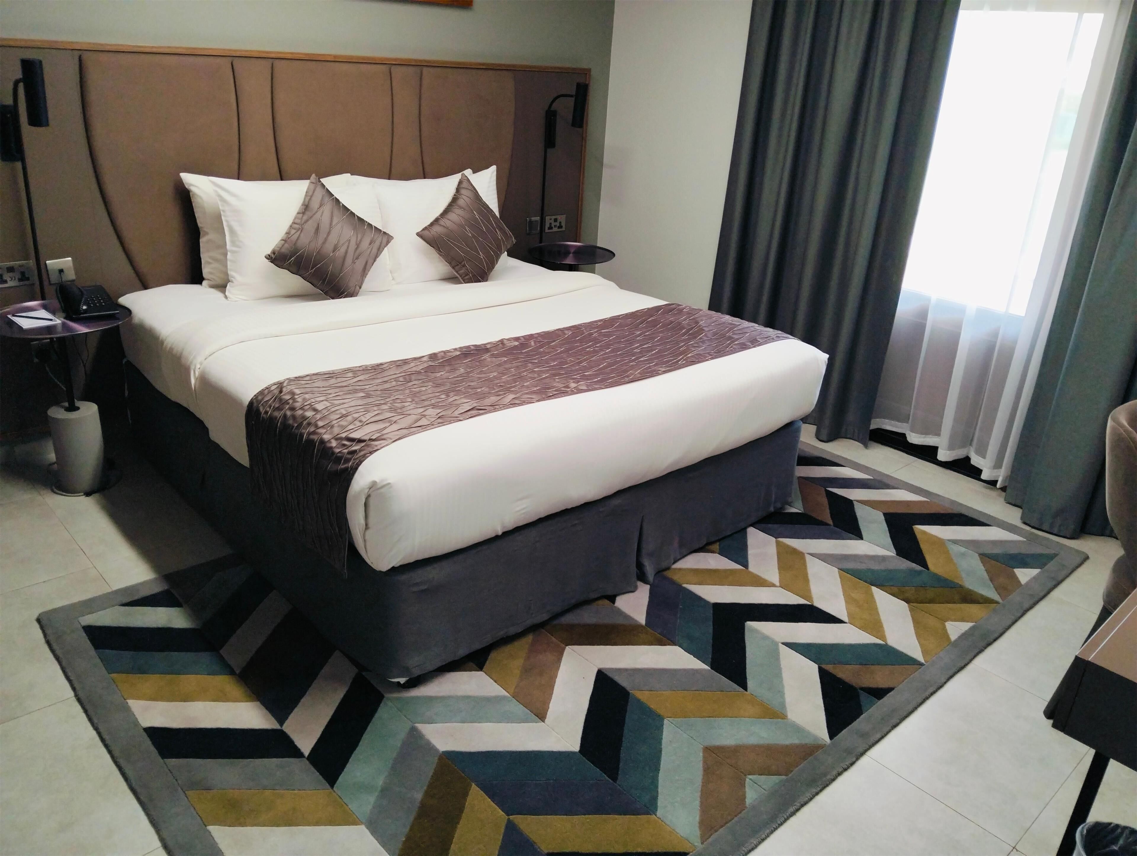 A hotel room with a large bed, a bedside table with a lamp, and a patterned rug.