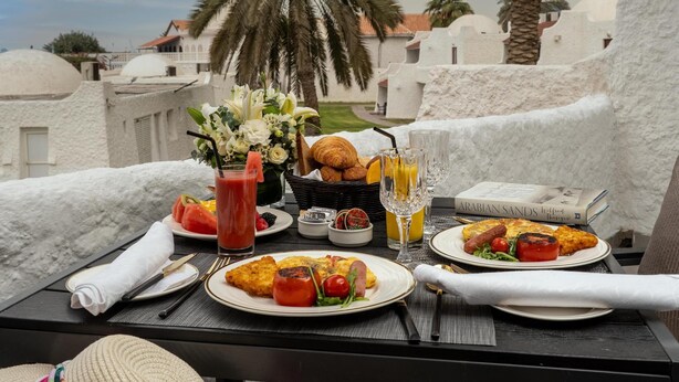 A table set for breakfast with a view of palm trees and buildings. - Marbella Resort Sharjah (Sharjah)