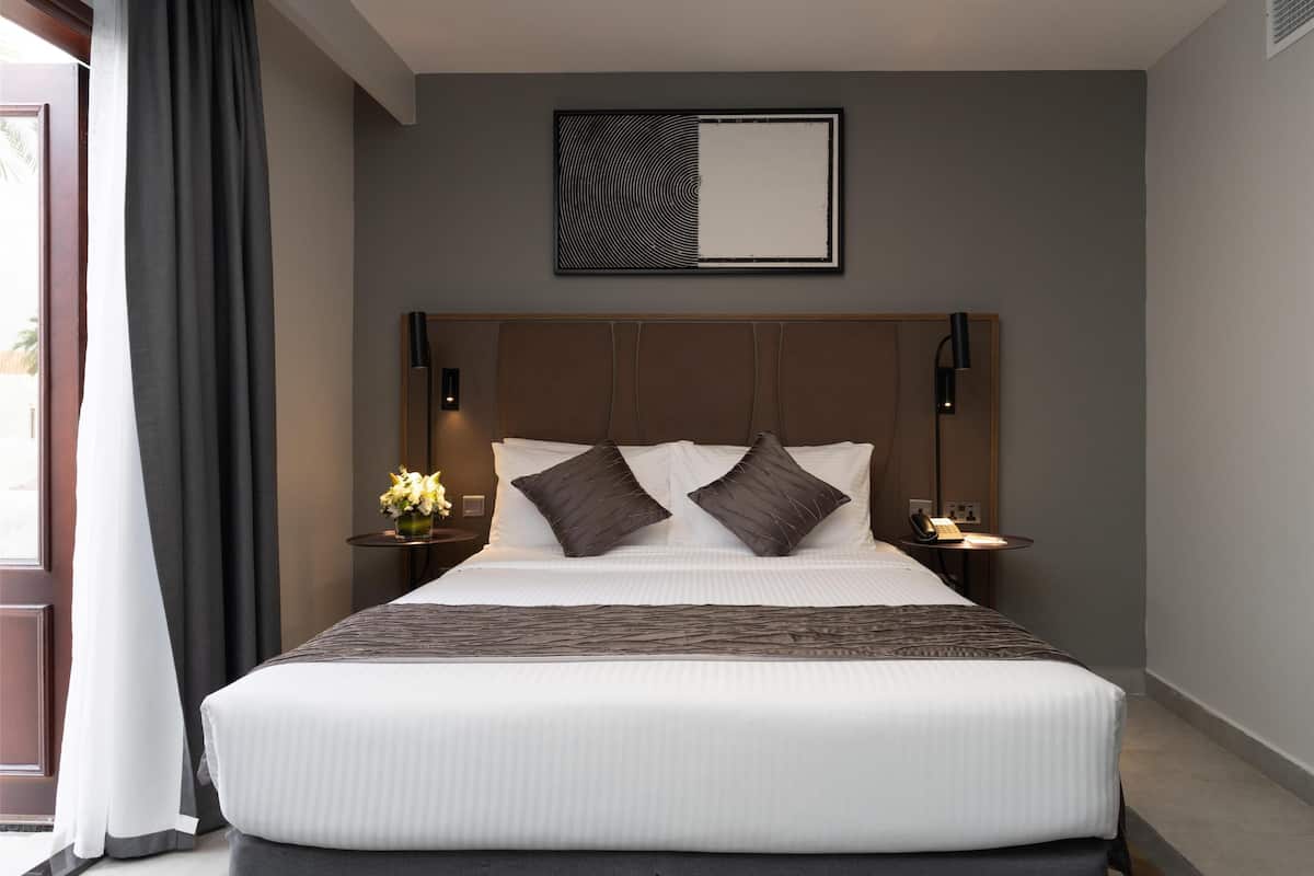 A large bed with a headboard, two bedside tables with lamps, and a wall-mounted artwork above the bed.