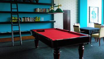 Une table de billard recouverte d’un drap rouge, entourée d’étagères, d’une échelle et d’une autre table de billard avec des chaises.