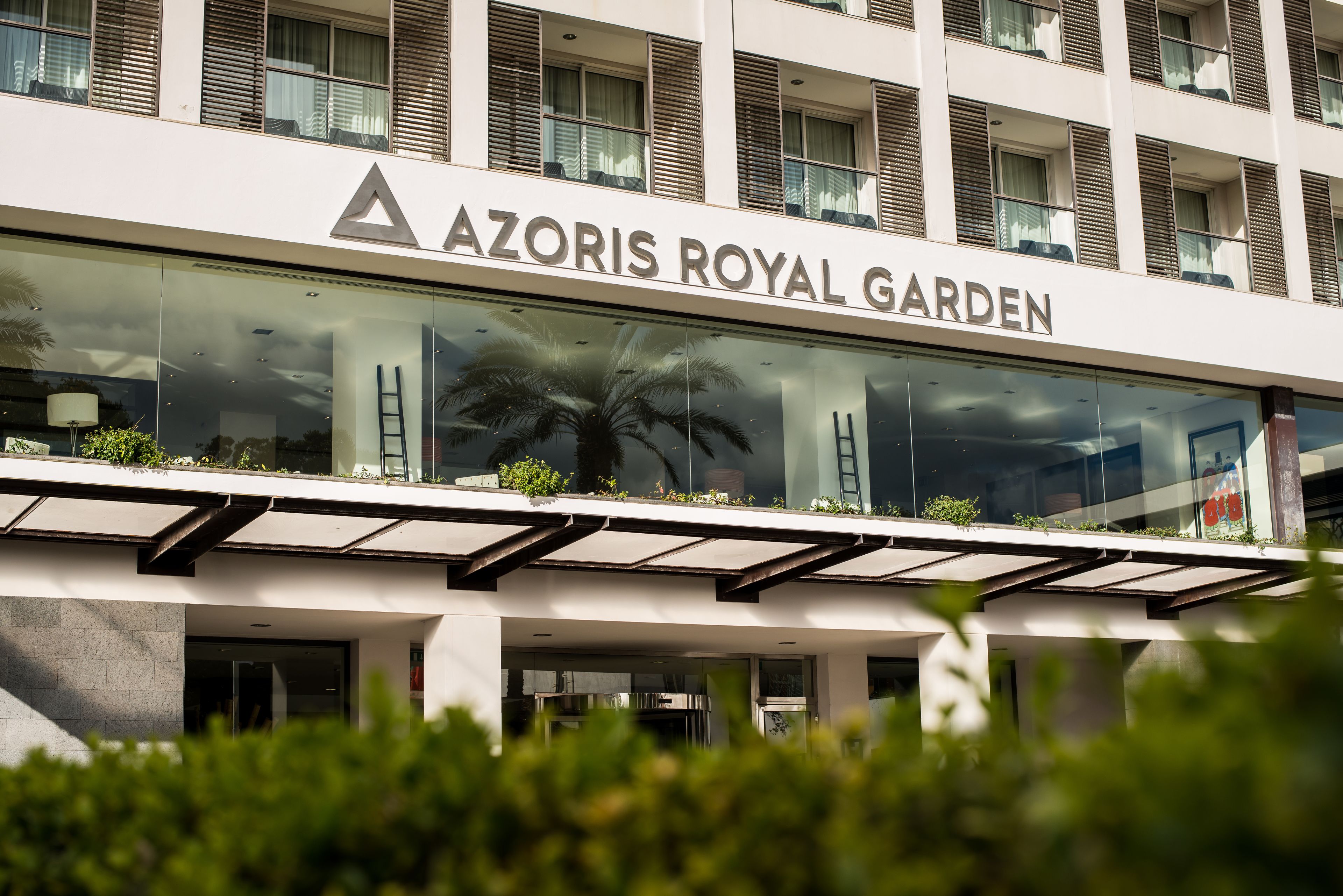 The exterior of Azoris Royal Garden hotel with a modern design, large glass windows, and a palm tree in the foreground.