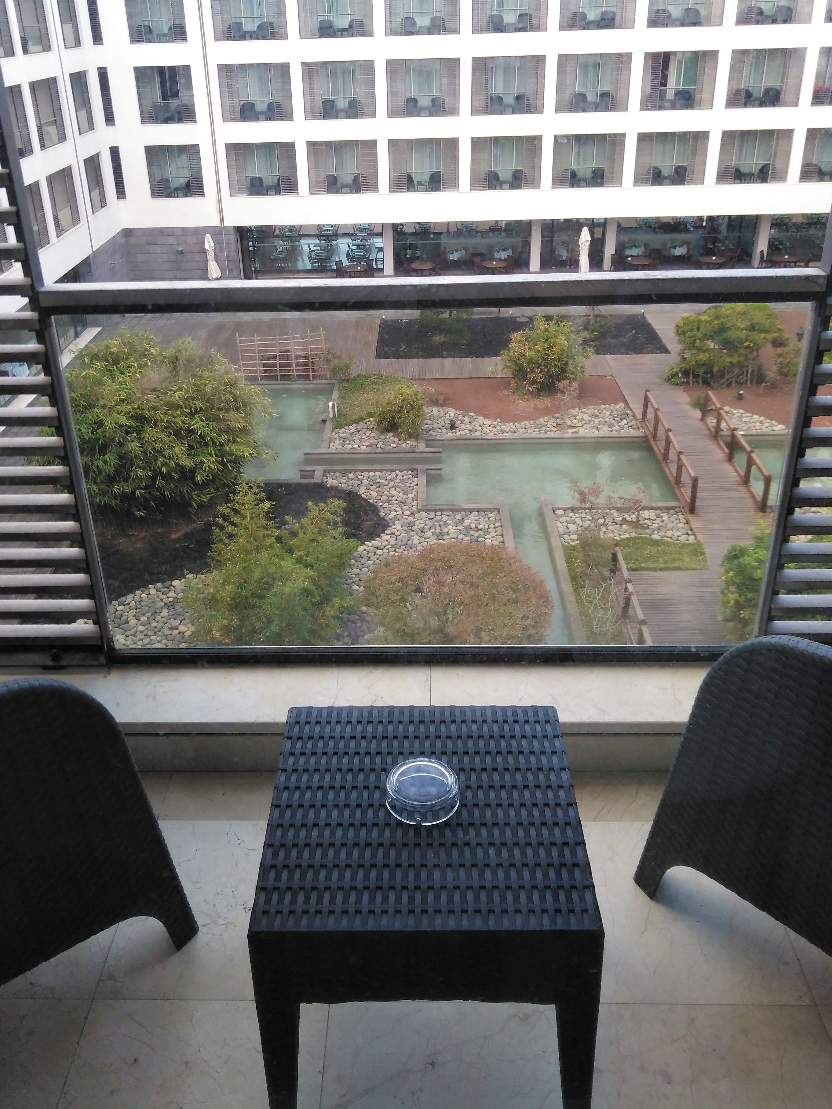 A balcony with a view of a landscaped garden, a small table, and two chairs.