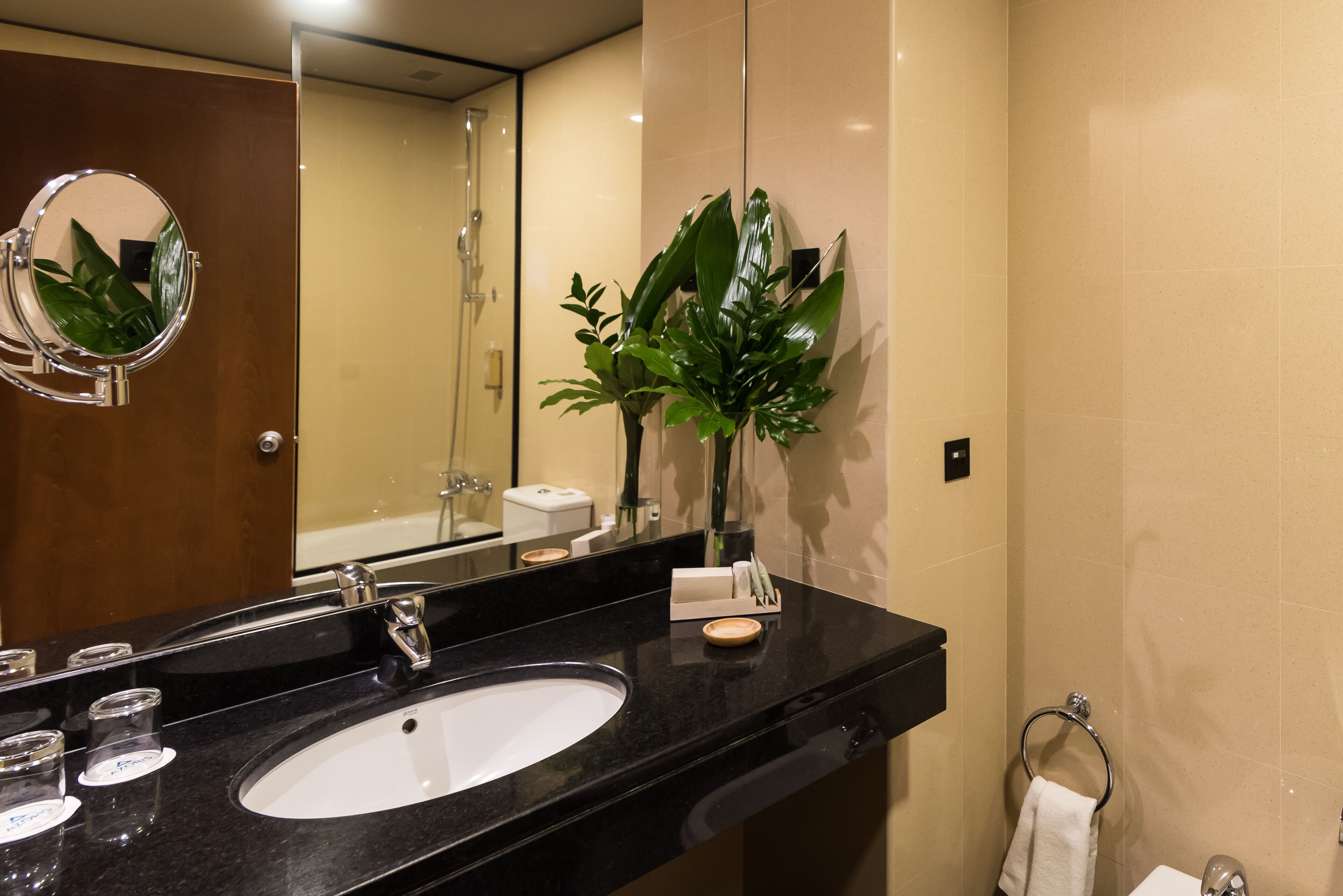 A modern bathroom with a black sink, a mirror, and a potted plant.