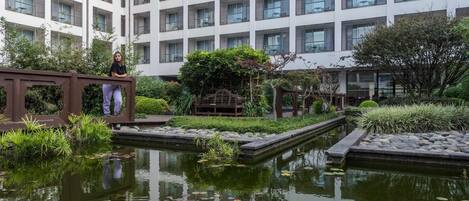 Un edificio moderno con múltiples ventanas y un patio con un pequeño estanque y vegetación.