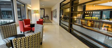 A modern hotel lobby with patterned chairs, a seating area, and a view of the bar area through a glass partition.