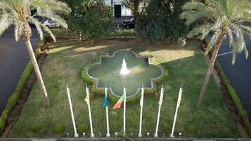Ein angelegter Gartenbereich mit einer zentralen Fontäne, Palmen und einer Reihe von Flaggen.